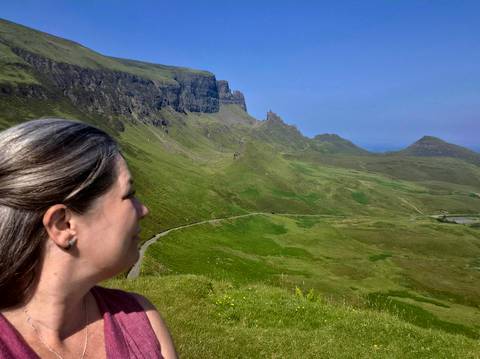       Traveler looks across the winding green ridges of the Quiraing on a clear summer day.
  