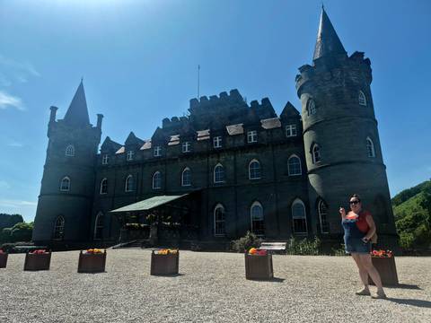       Traveler gestures toward dark stone Inveraray Castle silhouetted against a bright sky.
  