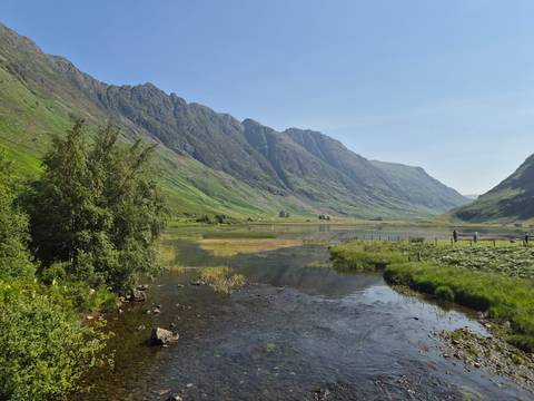       Serene Glencoe valley with steep green walls reflected in calm river wetlands.
  