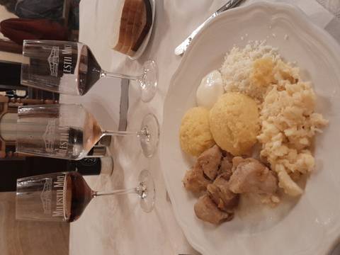       A Moldovan meal of meat, mamaliga polenta, cheese and wine is set before three tasting glasses on a white tablecloth.
  