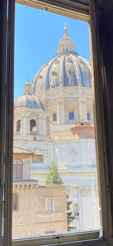       Architectural dome and colonnades of a grand basilica seen through an open window frame.
  