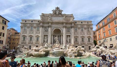       The ornate Trevi Fountain with crowds gathered around its turquoise waters and Baroque sculptures.
  