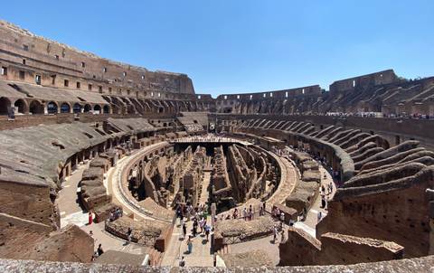       Panoramic interior view of the Colosseum’s tiered stone walls and arena floor filled with visitors.
  