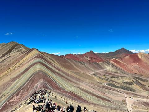       Vibrant striations of Rainbow Mountain undulate across a high Andean landscape under a brilliant blue sky.
  