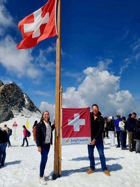       Visitors on a snowy peak holding a Swiss flag with glaciers and blue sky around
  
