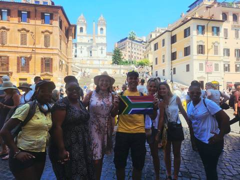       Small group holding a South African flag at Rome’s busy Spanish Steps on a sunny day
  