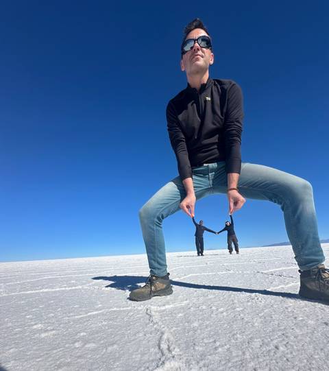       Creative perspective shot on the blinding-white Uyuni Salt Flats where a man appears to pinch two companions between his fingers under a deep blue sky.
  