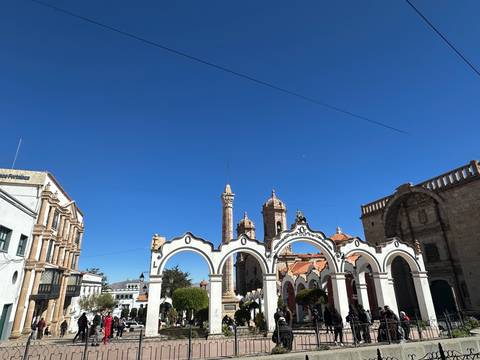       Elegant colonial arches and stone church towers rise against a vivid blue sky in a historic Bolivian plaza.
  