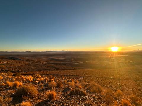       Golden sun sinks over the vast, high-altitude plains casting long rays across the rugged Bolivian landscape.
  