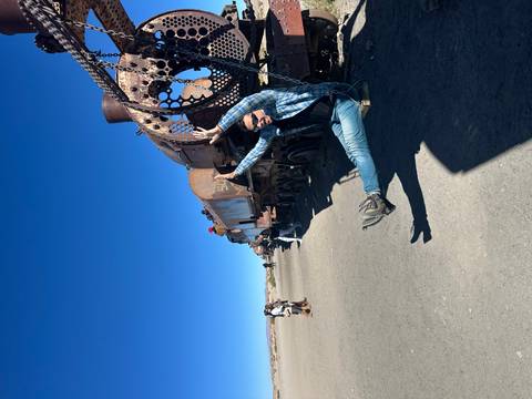       Traveler swings joyfully from the rusty frame of an old locomotive at Uyuni’s famous train graveyard while others explore nearby.
  