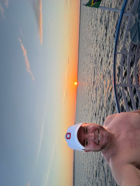       Partial selfie on a boat deck captures a vivid orange sunset over calm open water.
  