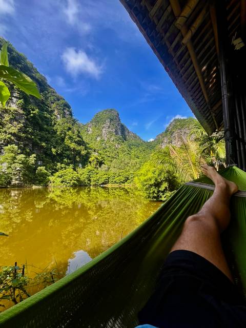       Relaxing view from a hammock over a calm green lake surrounded by steep jungle-covered cliffs
  