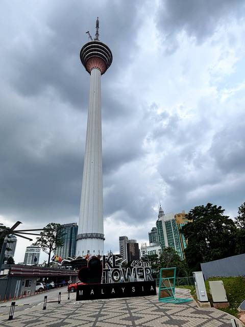       Tall KL Tower standing against a cloudy sky with city buildings in the background
  