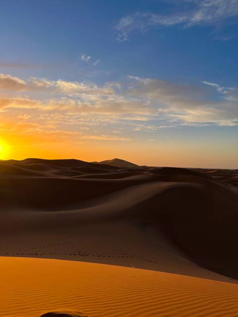       Golden sunset descends over sweeping sand dunes creating long shadows in the desert.
  