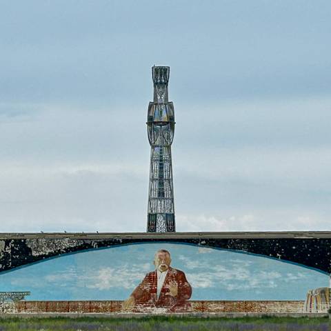       Tall steel communications tower rising above a mural of a cosmonaut against a cloudy sky.
  