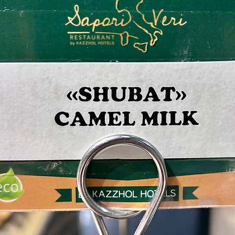       Close-up sign reading “SHUBAT CAMEL MILK” on a shop shelf.
  