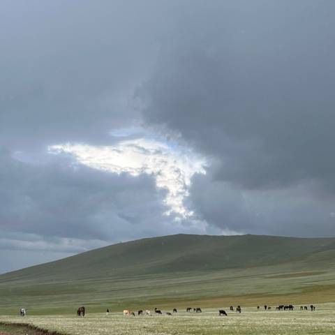       Moody sky with dramatic break in clouds over low green hill.
  