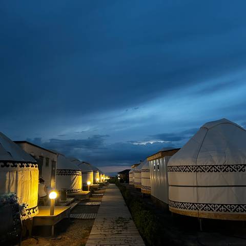       Row of illuminated yurts at twilight under a deep blue evening sky.
  