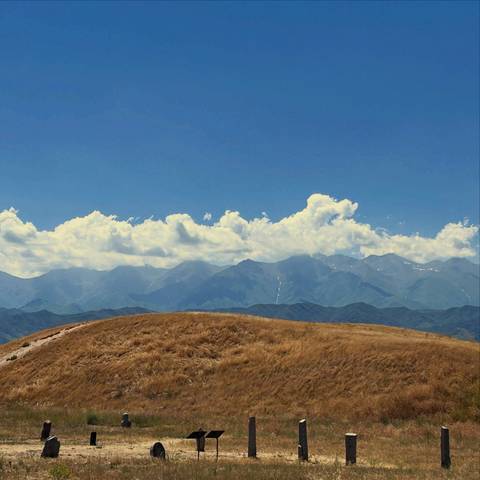       Golden grassy ridge with vast mountain range and fluffy clouds beyond.
  