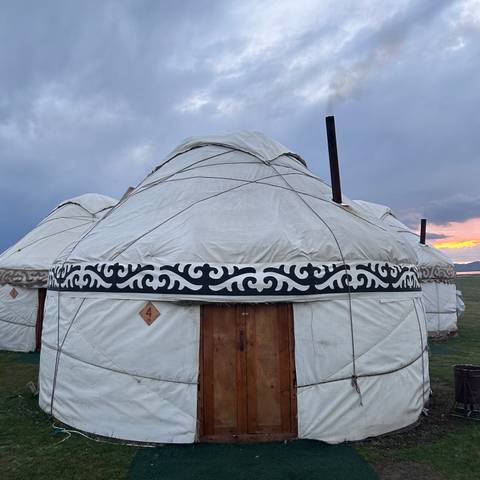       Close view of a traditional circular yurt with decorative black patterns at sunset.
  