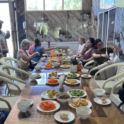       Tour group seated around a wooden table enjoying a spread of salads and local dishes.
  