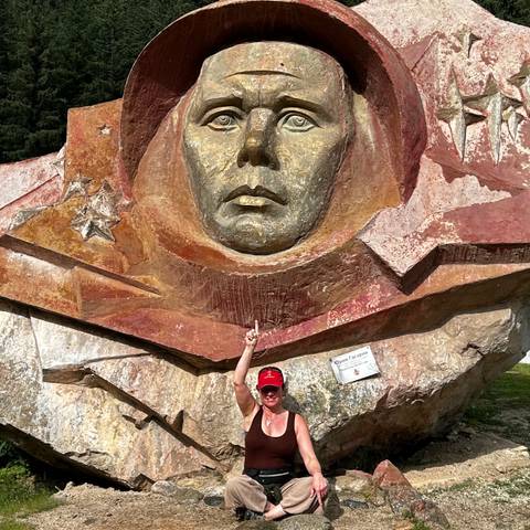       Visitor points up at the large golden Yuri Gagarin relief monument set in a forested area.
  
