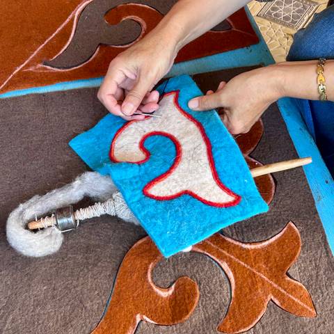       Close-up of hands stitching colourful felt on a traditional Kyrgyz textile piece
  