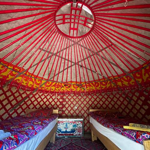       Interior view of a yurt roof with red wooden spokes and ornate patterns
  