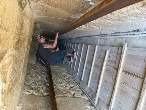       Visitor climbs a steep wooden staircase inside the narrow passage of a pyramid.
  