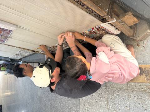       Tourist and local artisan knotting threads on a traditional carpet loom.
  
