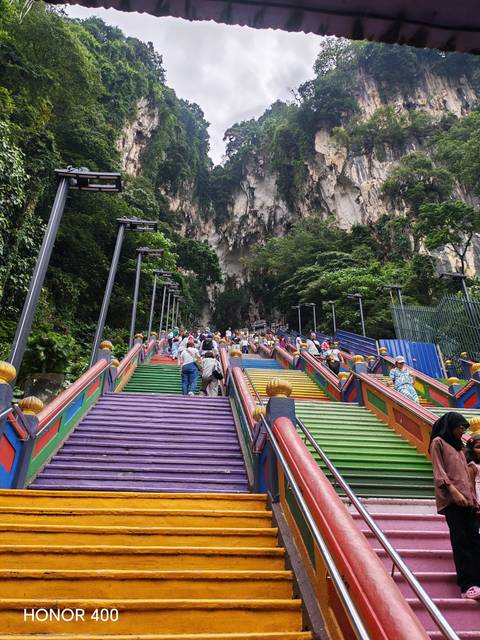       Colorful rainbow stairway leading up Batu Caves temple with crowds climbing the steps.
  