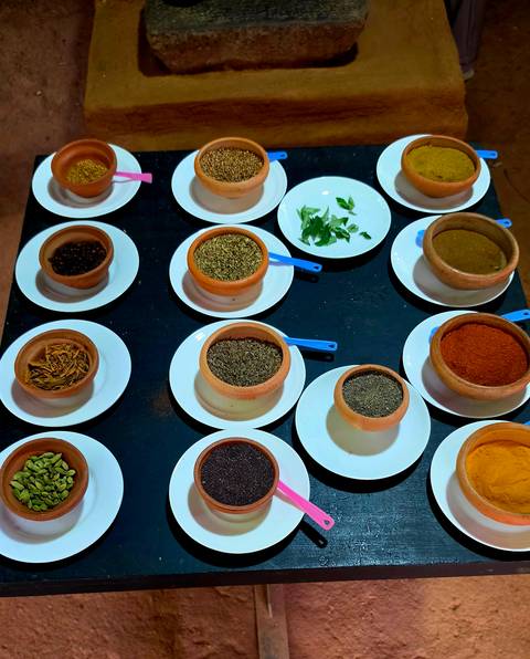       Overhead arrangement of clay bowls filled with assorted spices on white plates during a cooking class.
  