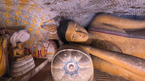      Colourful reclining Buddha statue inside a richly painted cave temple.
  