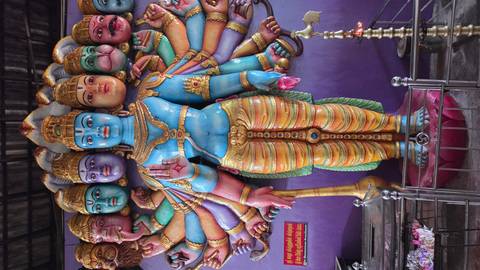       Vivid multi-armed Hindu deity sculpture with colourful expressive faces inside a shrine.
  