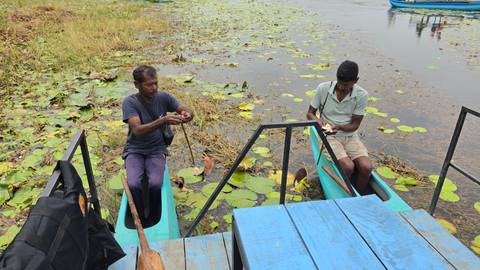       Two men prepare gear in small turquoise canoes among lily pads on a calm lagoon.
  