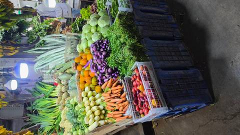       Brightly lit market stall stacked with colourful fresh vegetables including carrots, pumpkins and eggplants.
  