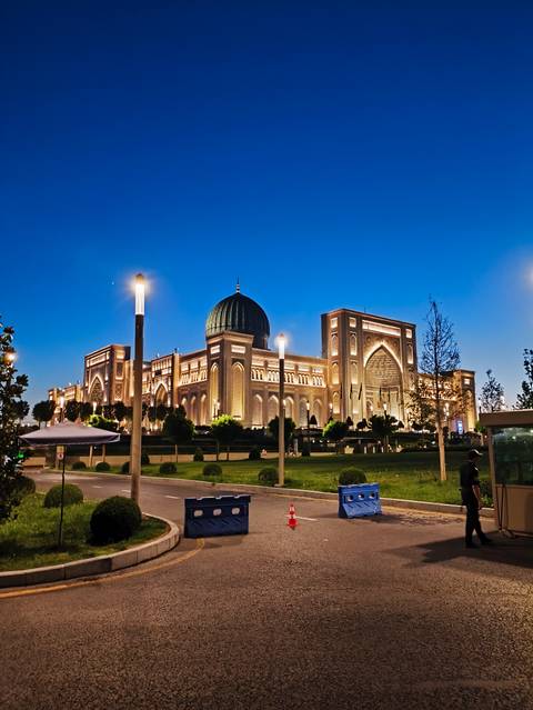       Grand illuminated palace-style building with a domed roof and intricate arches glowing at blue hour.
  