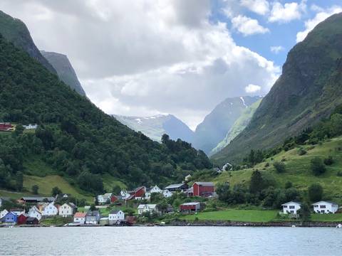       Picturesque Norwegian fjord village surrounded by verdant mountains and dramatic cloudy sky.
  