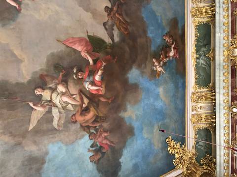       Close-up of an ornate baroque ceiling fresco depicting mythological figures amid dramatic clouds.
  