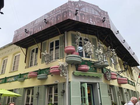       Quirky corner café building decorated with oversized pastel macaron sculptures and partially covered by renovation sheeting.
  