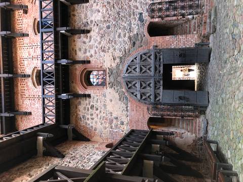       Interior courtyard of a red-brick medieval castle with a large arched wooden door; a single person seen through doorway.
  