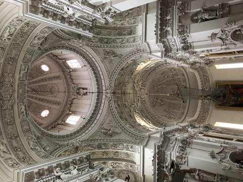       Lavishly decorated white baroque church ceiling with ornate stucco and central dome.
  