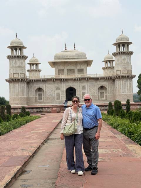       Smiling duo posing in front of ornate white marble tomb with intricate inlay work and minarets.
  
