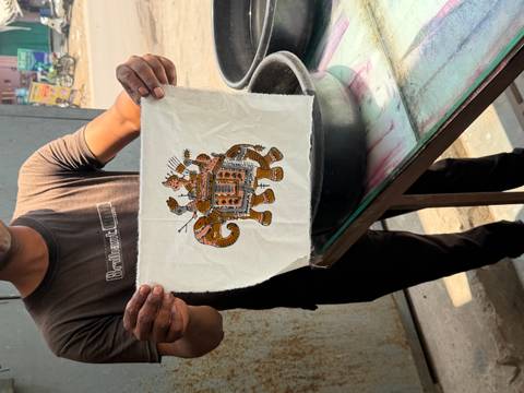       Artisan holding up a fabric square with an embroidered elephant design in a workshop.
  