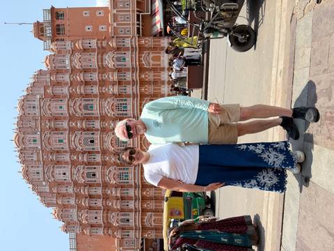       Couple standing in front of the ornate pink facade of Hawa Mahal on a sunny day.
  