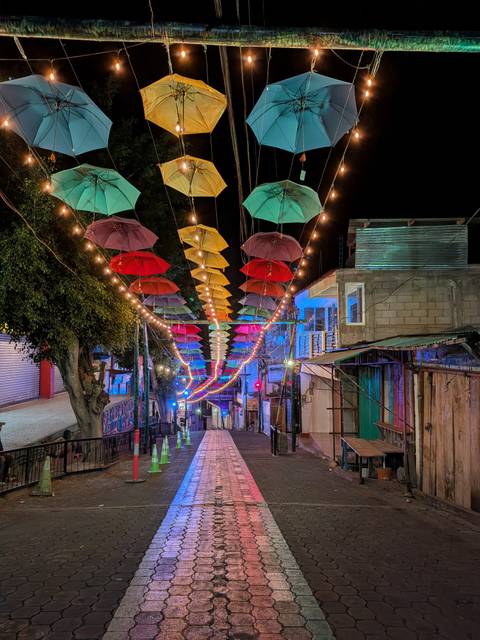       Colorful canopy of umbrellas and festive string lights illuminating a narrow street at night
  