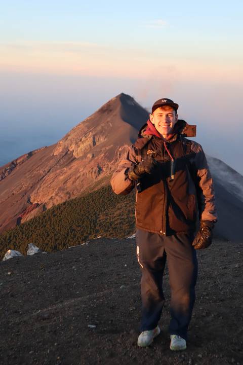       Solo hiker giving thumbs up on volcanic ridge with dramatic sunrise light on crater
  