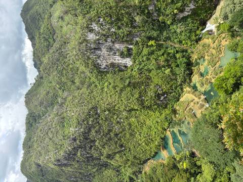       Lush green mountains with turquoise stepped pools and a river flowing through a deep jungle valley.
  