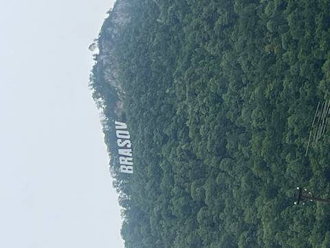       Green forested hillside with a large white 'BRASOV' sign visible through light mist.
  