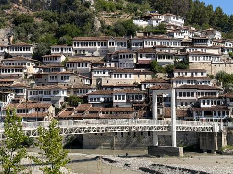       Berat’s hillside of white Ottoman houses stacked densely above a riverside bridge.
  